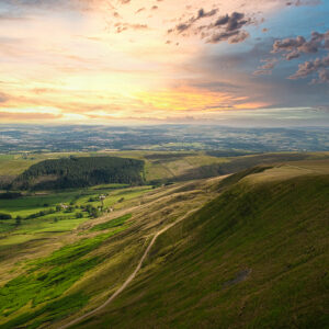 Breathtaking aerial view of rolling hills with a vibrant sunrise over a lush countryside landscape in Pendle Hill, England.