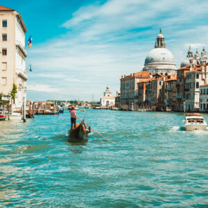 Venice, Italy. Gondolier looking for next tourists on Grand Canal. Basilica Santa Maria della Salute against blue sky and white clouds in background